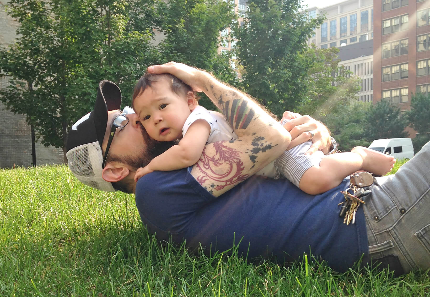 Justin on his back in the grass with his young son on his chest